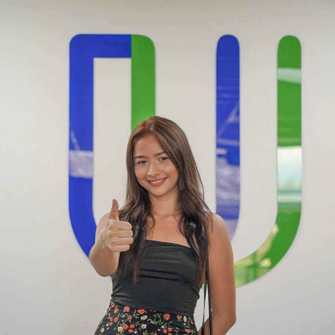 Estudiante sonriendo frente al logo de la UPES