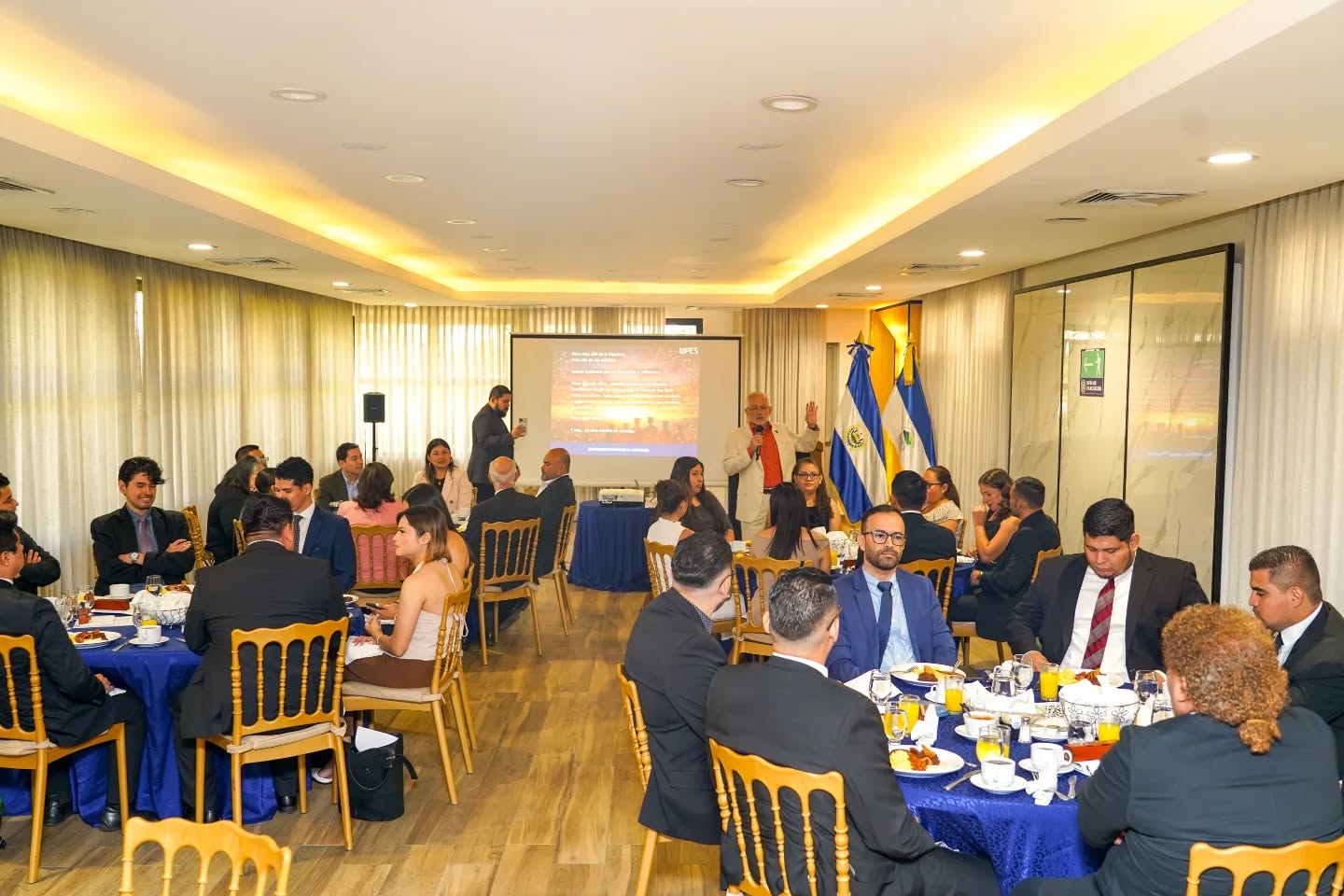 Asistentes en un desayuno institucional con proyección de fondo